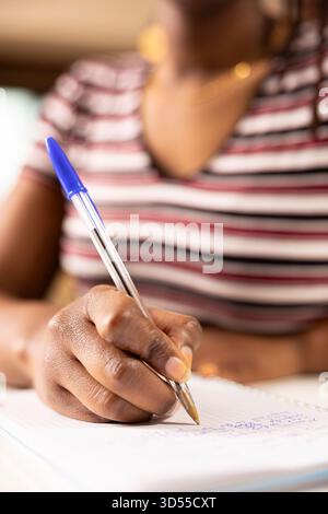 Black woman entrepreneur with pen in hand, writing project ideas on notebook during brainstorming moment. Close up of female individual organizing daily schedule and working remotely from home. Stock Photo