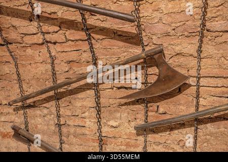 Transylvania, Romania - Oct 8, 2025: Old brick wall with various rusty medieval torture axes and tools hanging on chains, depicting historical Stock Photo