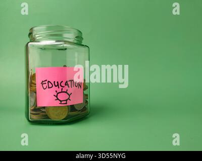 The image shows a glass jar filled with coins, with a pink sticky note on it that says EDUCATION. Stock Photo