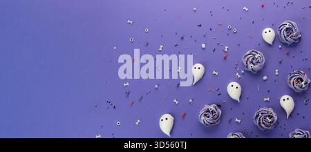 Delightful Halloween-themed treats are artistically placed on a dark purple surface, featuring ghost-shaped sweets and colorful sprinkles in various s Stock Photo