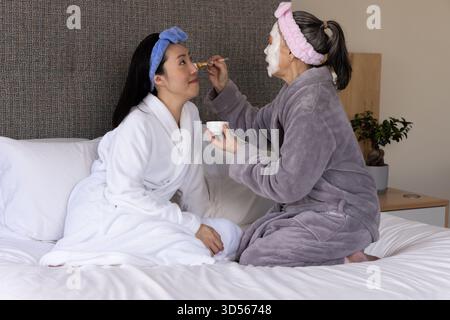 Asian mother and daughter engaging in skincare routine in cozy bedroom with brush and bowl Stock Photo