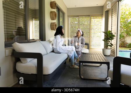 Asian adult mother and daughter sitting on modern sofa in indoor lounge, sharing gentle conversation Stock Photo