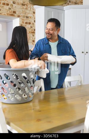 Asian couple chatting while doing chores in cozy kitchen, using laundry basket on table Stock Photo