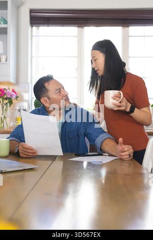Mature couple discussing finances at kitchen table, holding documents and coffee Stock Photo