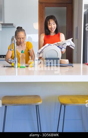 Washing and drying Asian mother and daughter at modern kitchen sink, with yellow sponge Stock Photo