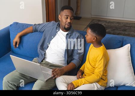Father and son talking on sofa while using laptop at home Stock Photo