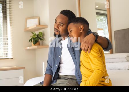 African American father and son sitting on bed, embracing and looking content Stock Photo