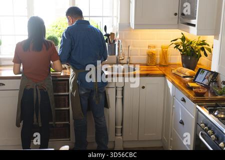 Asian couple preparing food in modern kitchen with cabinets, wooden countertop and pasta container Stock Photo