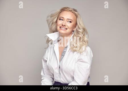 Attractive senior woman with a blonde hair looking side away on a grey background Stock Photo