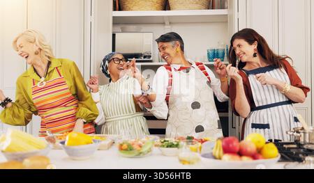 Cooking, kitchen and mature women dance for bonding, connection and culinary lesson. Happy, social reunion and senior friends with energy, fun and Stock Photo