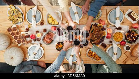 Thanksgiving, wine and cheers with hands of family for festive feast, celebration and dinner. Toast, alcohol drink and holiday season with above of Stock Photo