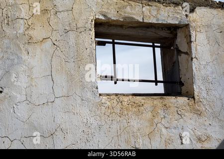Small window with metal bars in cracked wall showing rustic and worn textures. Stock Photo