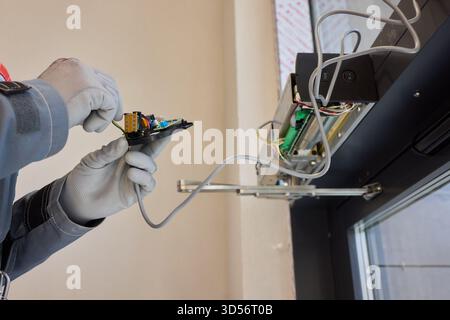 A technician is repairing an advanced automated door system with electrical tools Stock Photo
