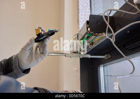 A technician is repairing an advanced automated door system with electrical tools Stock Photo