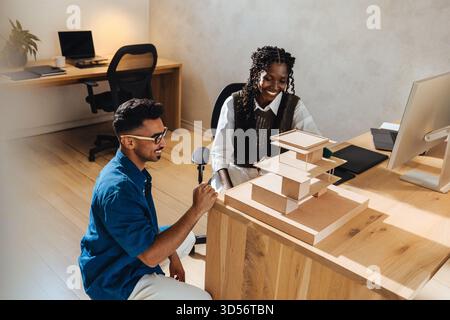 Two young architects collaborate on a scale architectural model at a workspace, showcasing teamwork, creativity, and modern design approaches in a pro Stock Photo