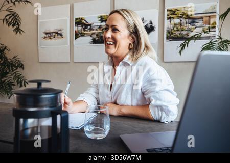Businesswoman sitting at a desk in an architect studio, surrounded by design concepts and a contemporary workspace. She appears engaged and focused, r Stock Photo