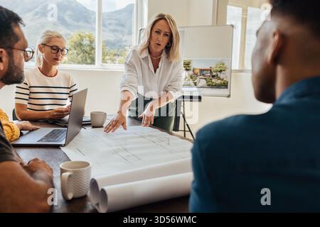A group of architects discussing design plans in a bright, modern office. The team includes men and women of various ages collaborating effectively. A Stock Photo