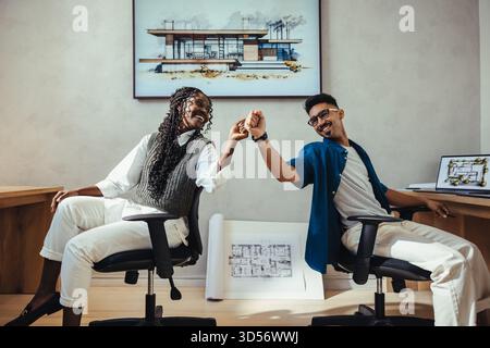 Young male and female professionals collaborating in a modern architecture studio, celebrating design success. Stock Photo