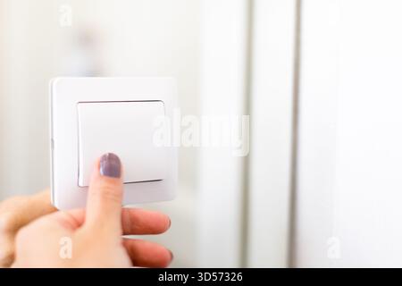 Turning on the light switch in a bright room with a hand reaching towards it Stock Photo