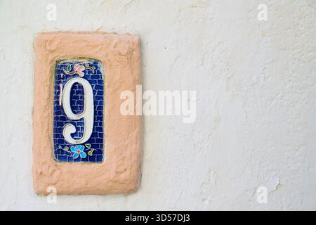 Decorative ceramic tile displaying the number nine on a textured wall, with copy space. Stock Photo