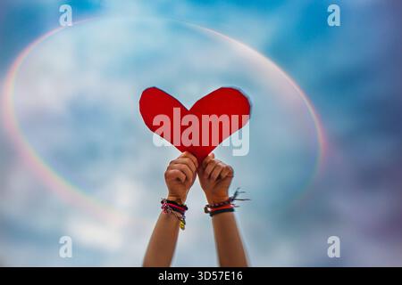 Hands Holding Red Heart in Sky with Rainbow background Stock Photo