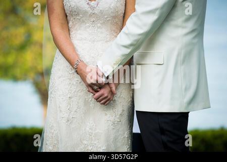 Bride and groom holding hands, dressed in lace and white suits Stock Photo