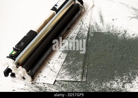 Printer toner cartridge placed on sheets of white paper and scattered with toner powder Stock Photo