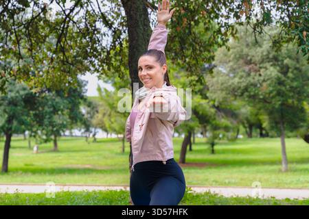 Sporty woman doing yoga warrior pose outdoors on mat in park smiling Stock Photo