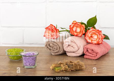 Spa composition with soft terry towels, red rose flowers, bowls with sea salt and soap on the wooden floor. Stock Photo