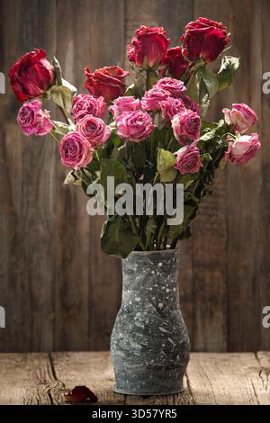 Dry pink roses in a gray handmade clay vase on a wooden background. Bouquet of dead roses, close-up. The concept of loneliness, age, sadness, old age Stock Photo
