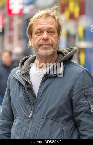 An elderly man with a beard stands on a city street against the background of pedestrians Stock Photo