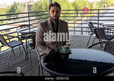 The man is sitting at a table on an outdoor patio or balcony, having coffee. Stock Photo