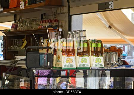 Valletta, Malta - 11.05.2025: Packs of bottled cider and glassware arranged on a glass bar counter beside a radio and cafe equipment Stock Photo