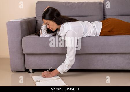 A woman is lying on the couch and writing in a notebook Stock Photo