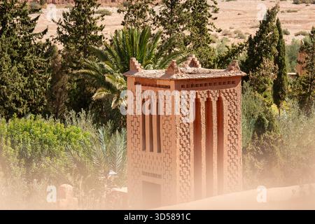 Clay-built architectural tower overlooking palm trees and ancient kasbah structures in Ouarzazate. Stock Photo