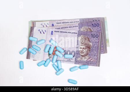 Blue capsules scattered over several Malaysian Ringgit banknotes symbolizing healthcare cost or pharmaceutical expenses in Malaysia, asia Stock Photo