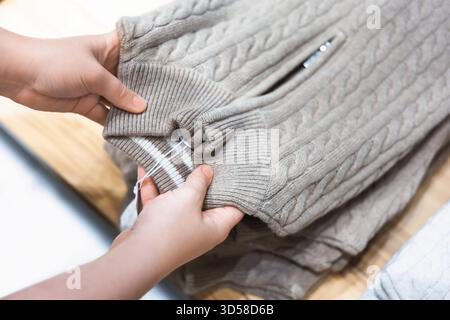 Hands holding a beige cable knit sweater with a ribbed cuff and zipper detail on a wooden surface. High quality photo Stock Photo