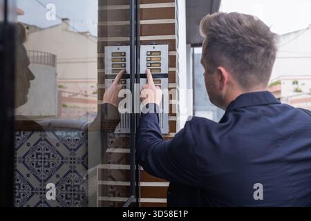 A Young Man Visiting and Pressing the Intercom Button to Be Let In Stock Photo