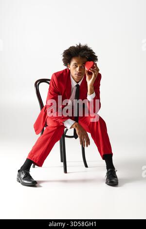 A charming young man in an elegant red outfit sits confidently, holding a small object. Stock Photo