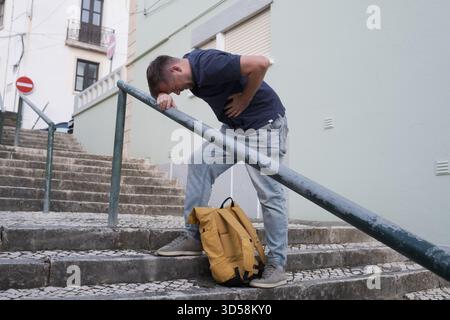 A Young Man Having a Heart Attack on the Street, Standing on the Stairs and Holding His Chest  Stock Photo