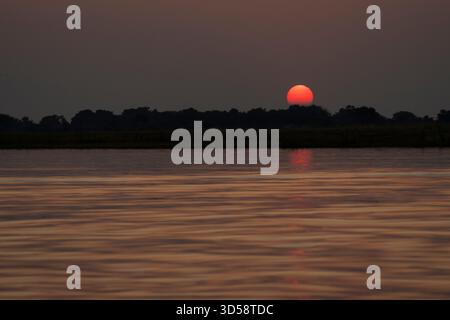 African sunset over the Chobe river in Botswana. Sun glows in beautiful red colour. Kasane, Botswana, Africa Stock Photo