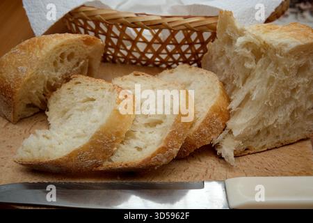 Freshly baked bread sits sliced on a wooden board beside a knife. Stock Photo