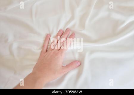 Female hand gently touching white silky sheet Stock Photo