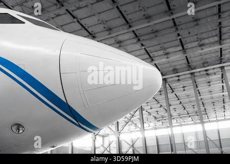 Nose of white aircraft in a hangar. White airplane with blue stripe on the front part of the fuselage. Stock Photo