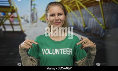 Woman wearing a shirt is pointing in a studio at volunteer blonde young wearing a tshirt and green earring. Stock Photo