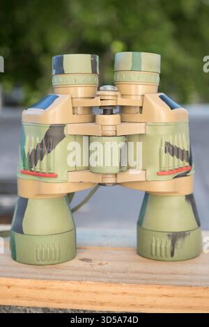 camouflaged binoculars on a wooden surface outdoors Stock Photo