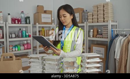 Young woman in a reflective vest works at a charity center organizing supplies indoors, emphasizing volunteer spirit and efficiency with her uniform a Stock Photo