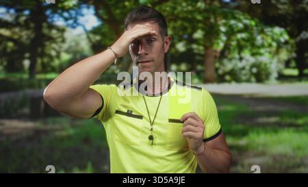 Man referee holding yellow card wearing whistle on lanyard in forest daylight; rule enforcement frustration. Stock Photo