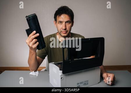 Portrait of skilled computer technician replacing toner cartridge in laser printer during maintenance service, holding new cartridge and looking at Stock Photo