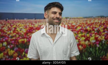 Man wearing a white shirt smiling in a vibrant tulip field studio setting while tilting his head gently; joy optimism. Stock Photo